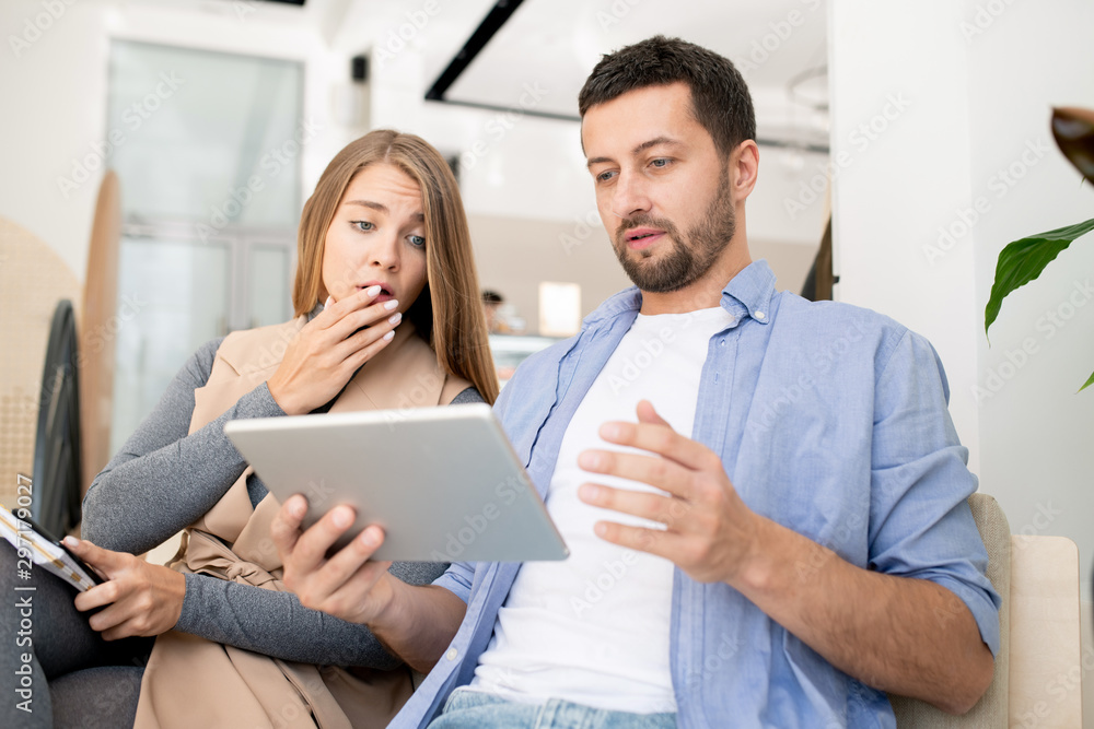 Young worried couple looking at touchpad display while surfing in the net Young worried couple looking at touchpad display while surfing in the net