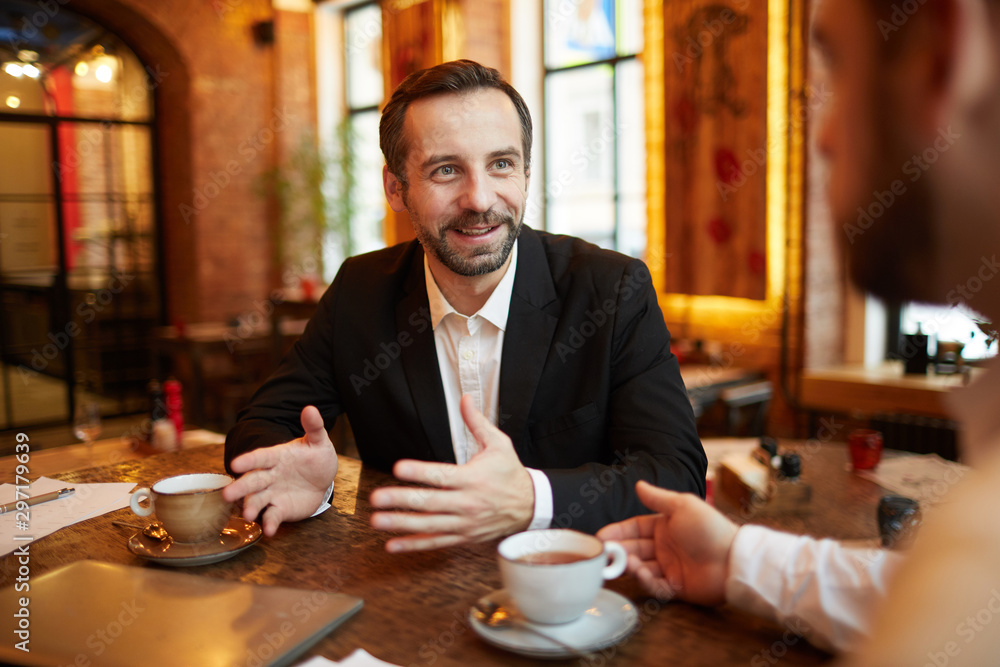Portrait of successful mature businessman pitching idea to partner and smiling during meeting in luxurious cafe