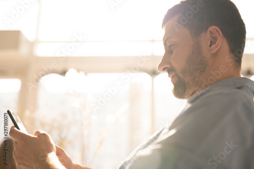 Young serious businessman with smartphone scrolling through information