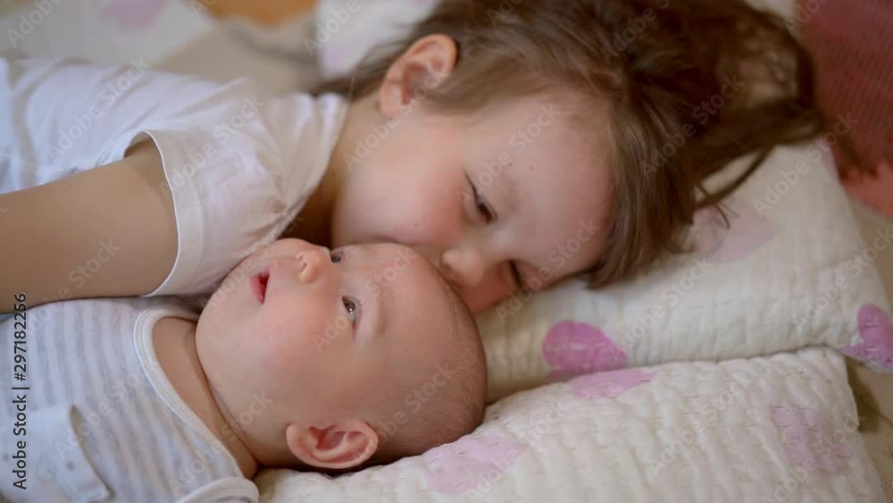 Older sister take care of the newborn baby sister. two little girls are lying on the bed. Concept of love and child care. Older sister take care of the newborn baby sister. two little girls are lying on the bed. Concept of love and child care.