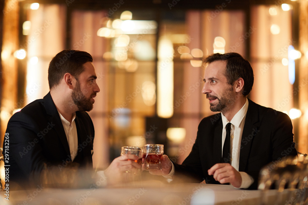 Side view portrait of two business partners drinking whiskey while enjoying dinner in luxury restaurant after work