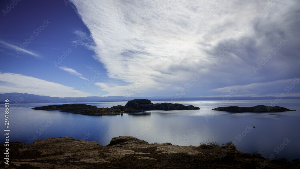 Small rocky island in front of the village of Chiloe. This island is located in the General Carrera Lake in Patagonia, Chile. The background is full of mountains and clouds. Small rocky island in front of the village of Chiloe. This island is located in the General Carrera Lake in Patagonia, Chile. The background is full of mountains and clouds.