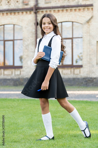 Lesson learnt. Happy small girl back to school. Small kid hold book and pen outdoor. Cute small child smile at school time. Adorable small schoolchild with long brunette hair in formal wear photo