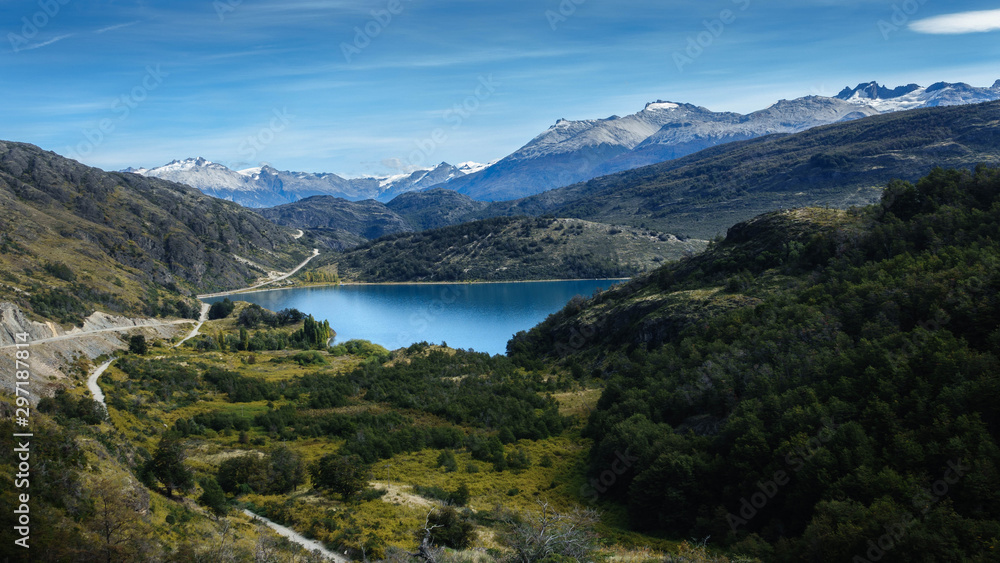 Characteristic landscape of the Andes mountain range in Argentine or Chilean Patagonia. There is a beautiful lake, a forest, great mountains and a dirt road.