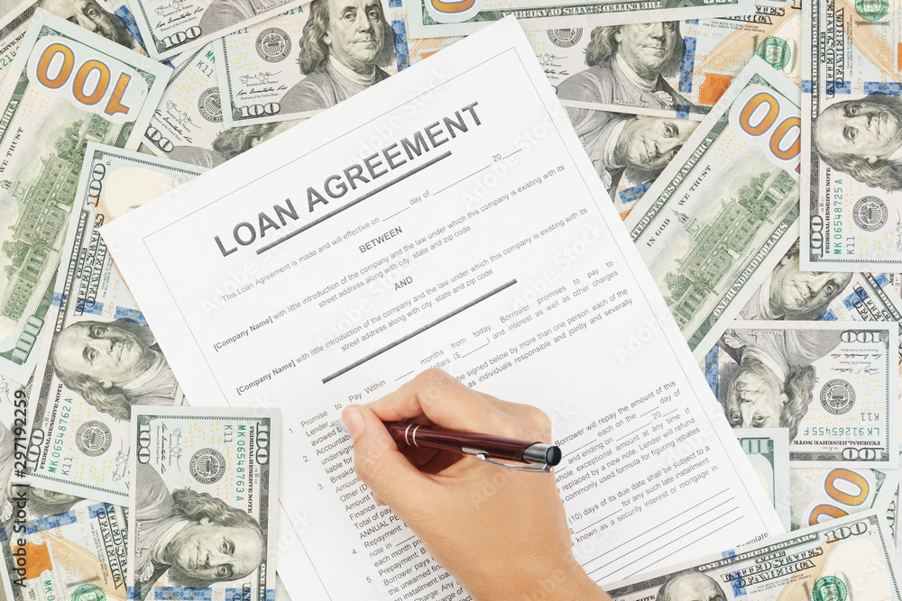 Obraz premium A woman reads and signs a loan agreement on the background of dollar bills. Concept of loan, mortgage, installment. Top view.