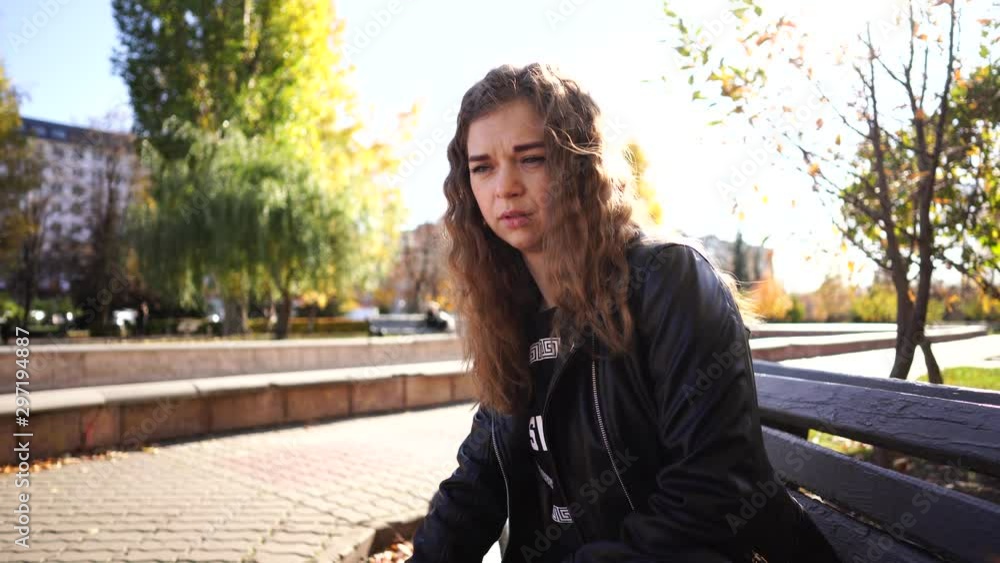 A young beautiful woman in casual clothes is sitting on a bench in autumn park. A young beautiful woman in casual clothes is sitting on a bench in autumn park.