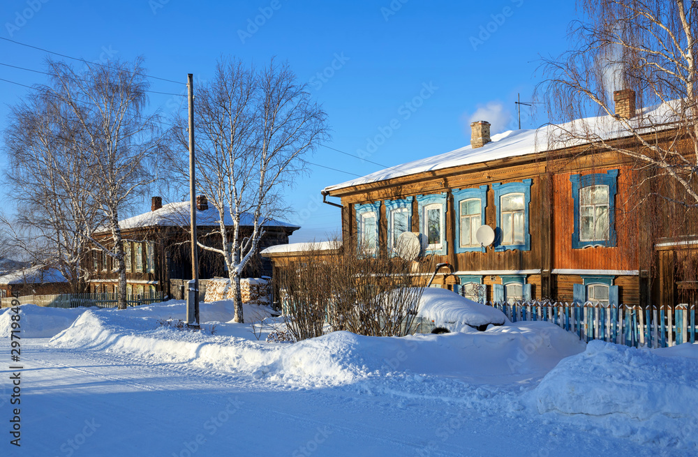 Snow-covered village street with old wooden residential houses. Village of Visim, Ural, Russia