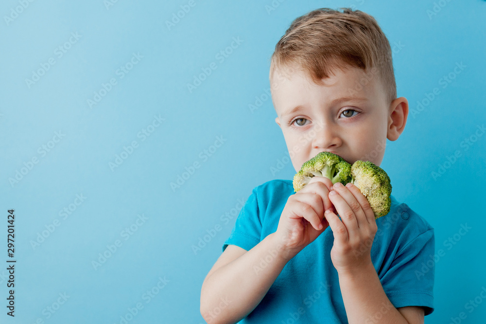 Little kid holding broccoli in his hands on blue background. Vegan and healthy concept Little kid holding broccoli in his hands on blue background. Vegan and healthy concept