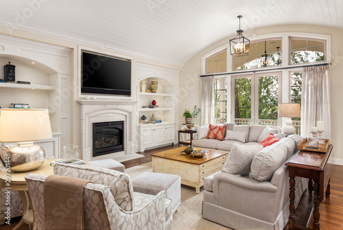 Beautiful living room in new traditional style luxury home. Features vaulted ceilings, fireplace with wall mounted tv, french doors leading outside, and elegant furnishings.