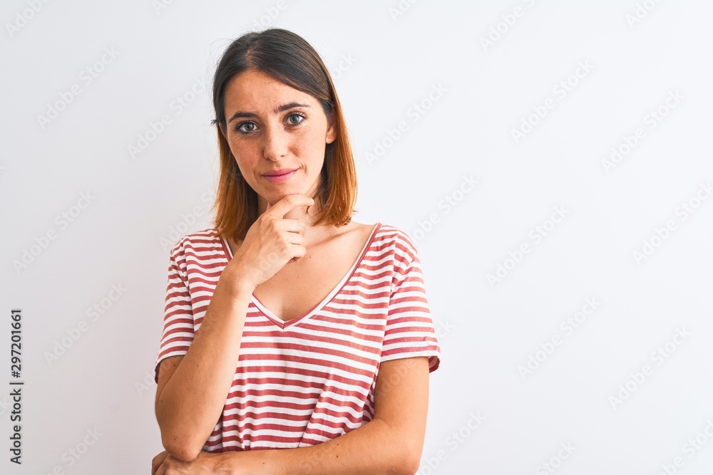 Beautiful redhead woman wearing casual striped red t-shirt over isolated background looking confident at the camera with smile with crossed arms and hand raised on chin. Thinking positive. Beautiful redhead woman wearing casual striped red t-shirt over isolated background looking confident at the camera with smile with crossed arms and hand raised on chin. Thinking positive.