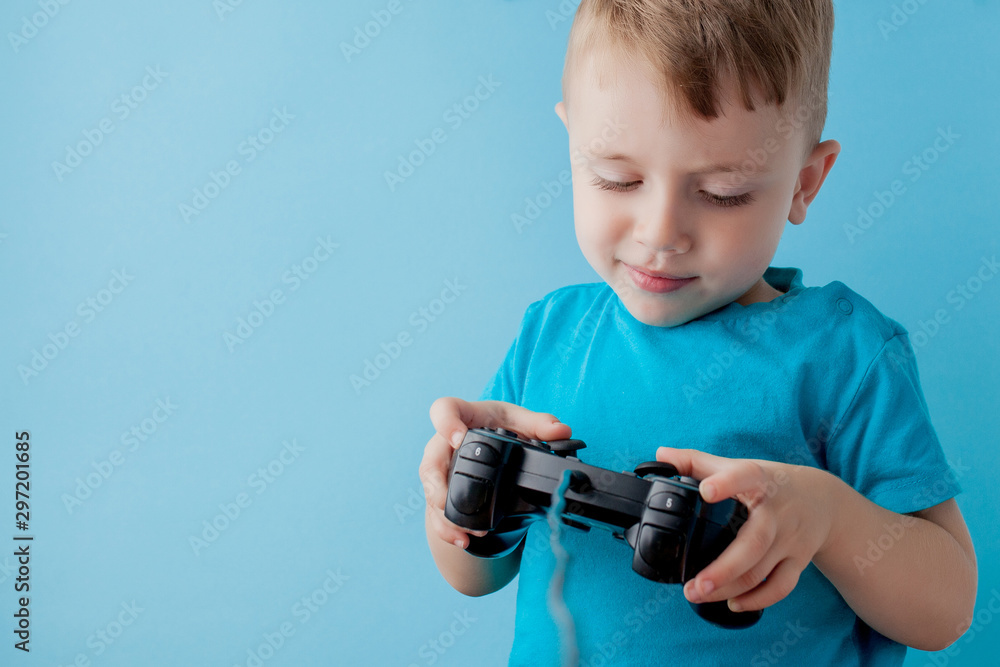 Little kid boy 2-3 years old wearing blue clothes hold in hand joystick for gameson blue background children studio portrait. People childhood lifestyle concept. Mock up copy space
