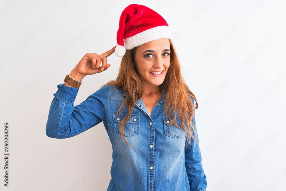 Young beautiful redhead woman wearing christmas hat over isolated background Smiling pointing to head with one finger, great idea or thought, good memory Young beautiful redhead woman wearing christmas hat over isolated background Smiling pointing to head with one finger, great idea or thought, good memory