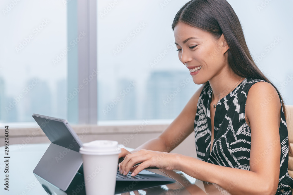 Asian businesswoman working typing on laptop computer writing online at office desk. Freelance remote worker writer at home or customer service support. Business woman lifestyle by window.