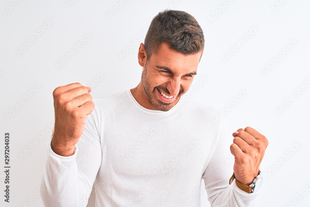Young handsome man wearing white shirt over isolated background very happy and excited doing winner gesture with arms raised, smiling and screaming for success. Celebration concept. Young handsome man wearing white shirt over isolated background very happy and excited doing winner gesture with arms raised, smiling and screaming for success. Celebration concept.