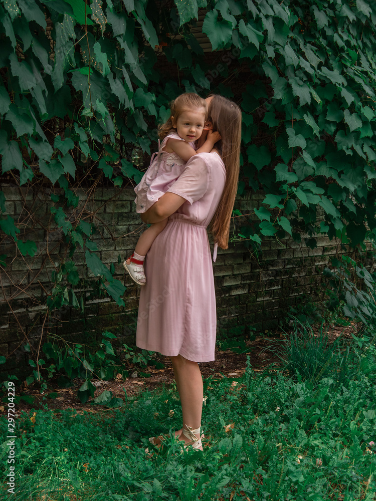Mom and daughter walk and play in the park. Dressed in dresses. Sunny day, weekend in a city park. Mom and daughter walk and play in the park. Dressed in dresses. Sunny day, weekend in a city park.