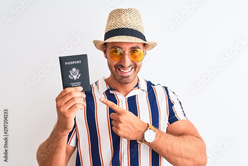 Young tourtist man wearing summer hat and holding USA passport over isolated background very happy pointing with hand and finger photo