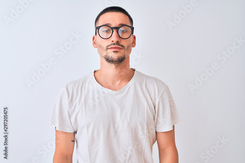 Young handsome man wearing glasses and standing over isolated background with serious expression on face. Simple and natural looking at the camera. © Krakenimages.com