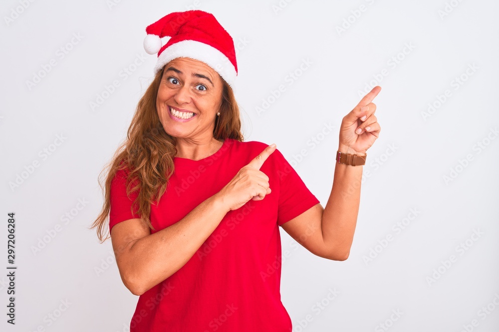 Middle age mature woman wearing christmas hat over isolated background smiling and looking at the camera pointing with two hands and fingers to the side. Middle age mature woman wearing christmas hat over isolated background smiling and looking at the camera pointing with two hands and fingers to the side.