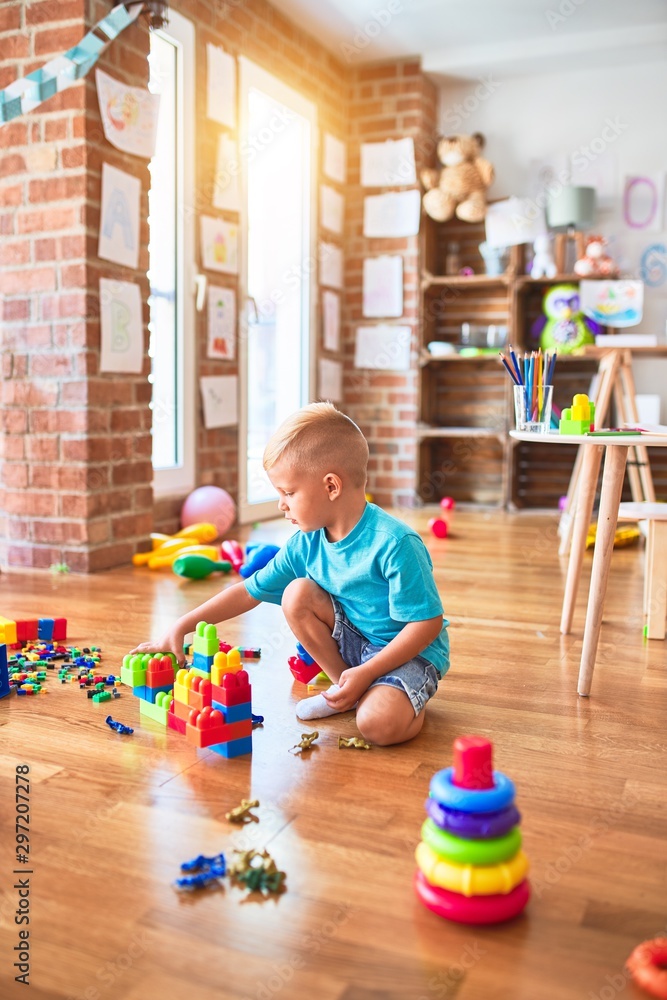 Fototapeta premium Young caucasian kid playing at kindergarten with toys. Preschooler boy happy at playroom.
