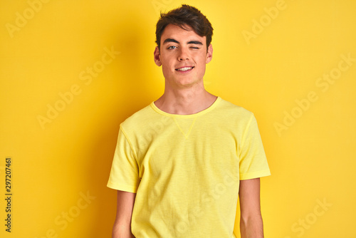 Teenager boy wearing yellow t-shirt over isolated background winking looking at the camera with sexy expression, cheerful and happy face.
