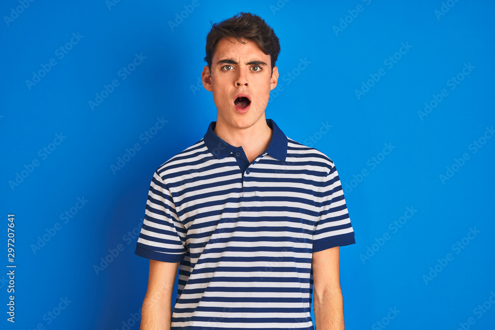 Teenager boy wearing casual t-shirt standing over blue isolated background In shock face, looking skeptical and sarcastic, surprised with open mouth Teenager boy wearing casual t-shirt standing over blue isolated background In shock face, looking skeptical and sarcastic, surprised with open mouth