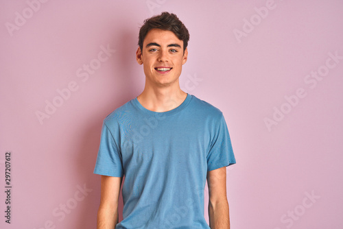 Teenager boy wearing casual t-shirt standing over blue isolated background with a happy and cool smile on face. Lucky person.