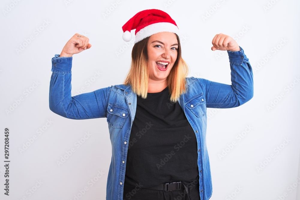Young beautiful woman wearing Christmas Santa hat standing over isolated white background showing arms muscles smiling proud. Fitness concept. Young beautiful woman wearing Christmas Santa hat standing over isolated white background showing arms muscles smiling proud. Fitness concept.