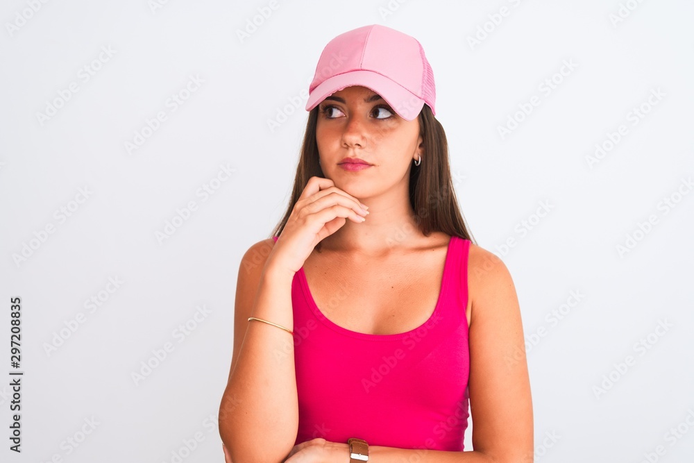 Young beautiful girl wearing pink casual t-shirt and cap over isolated white background with hand on chin thinking about question, pensive expression. Smiling with thoughtful face. Doubt concept. Young beautiful girl wearing pink casual t-shirt and cap over isolated white background with hand on chin thinking about question, pensive expression. Smiling with thoughtful face. Doubt concept.