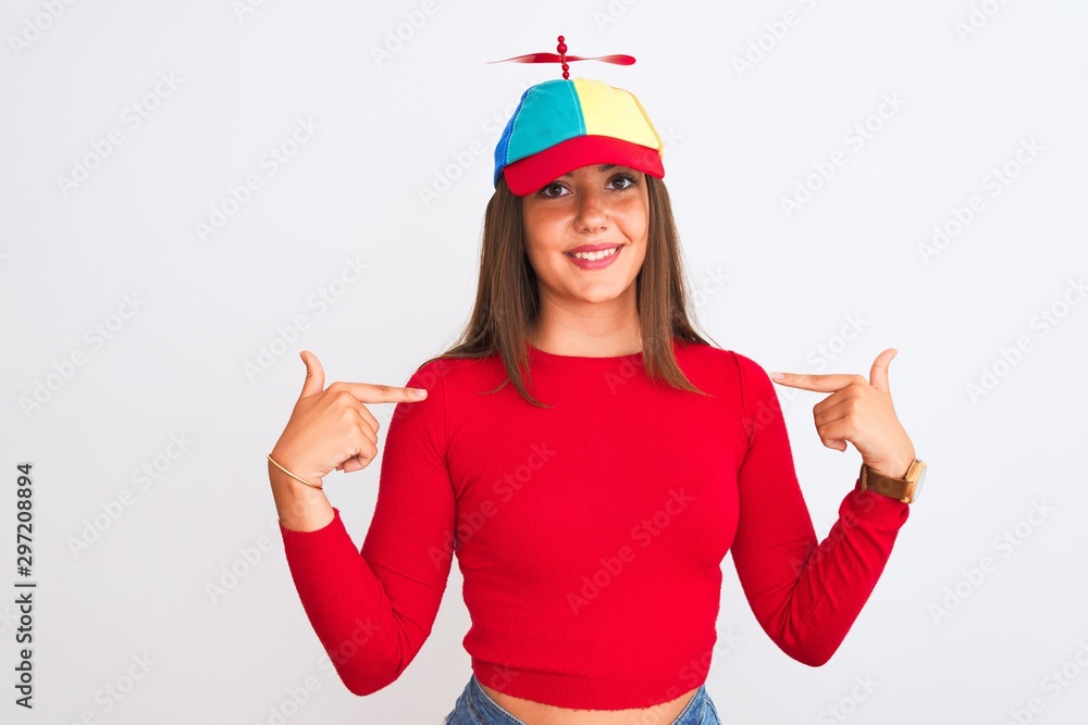 Young beautiful girl wearing fanny cap with propeller standing over isolated white background looking confident with smile on face, pointing oneself with fingers proud and happy. Young beautiful girl wearing fanny cap with propeller standing over isolated white background looking confident with smile on face, pointing oneself with fingers proud and happy.