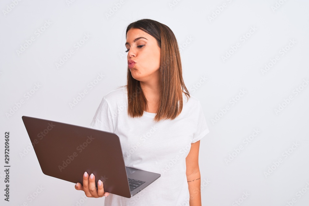 Beautiful young woman working using computer laptop over white background looking at the camera blowing a kiss on air being lovely and sexy. Love expression. Beautiful young woman working using computer laptop over white background looking at the camera blowing a kiss on air being lovely and sexy. Love expression.