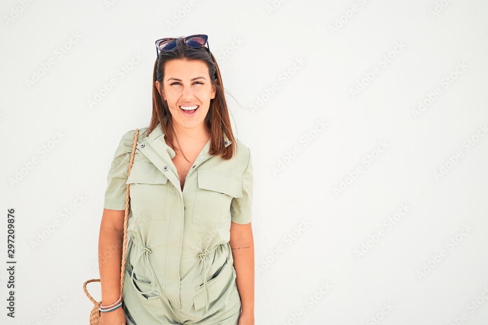 Beautiful girl leaning on white wall, young friendly woman smiling happy on a sunny day of summer Beautiful girl leaning on white wall, young friendly woman smiling happy on a sunny day of summer