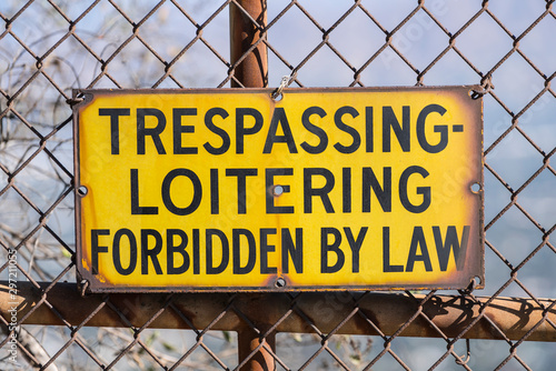 Old Trespassing and Loitering Forbidden by Law sign on rusty chain link fence. 