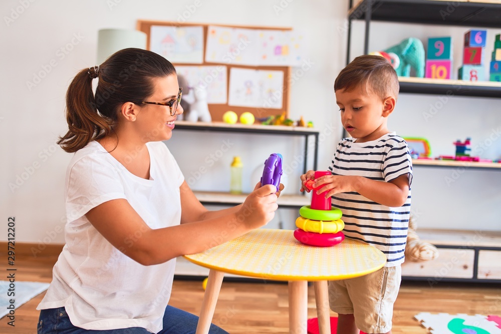 Beautiful teacher and toddler boy building pyramid with hoops bolcks at kindergarten Beautiful teacher and toddler boy building pyramid with hoops bolcks at kindergarten