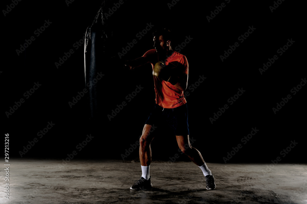 Male boxer training with punching bag in dark sports hall