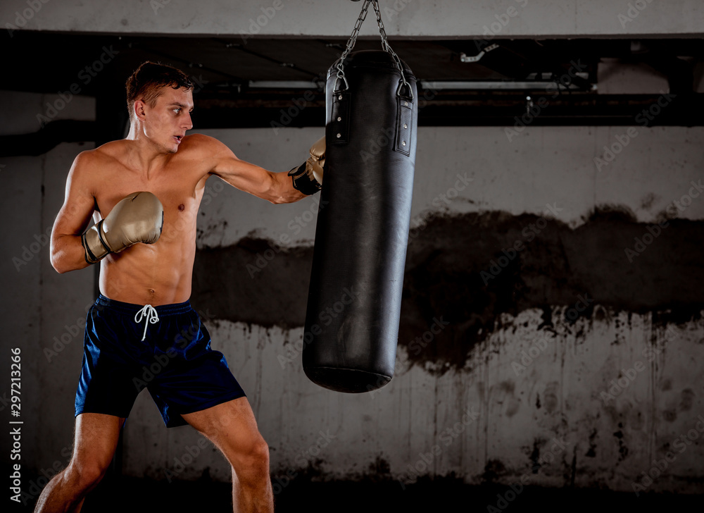 Athletic man in black sportswear training to box with punching bag