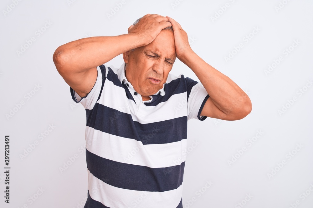 Senior grey-haired man wearing casual striped polo standing over isolated white background suffering from headache desperate and stressed because pain and migraine. Hands on head. Senior grey-haired man wearing casual striped polo standing over isolated white background suffering from headache desperate and stressed because pain and migraine. Hands on head.