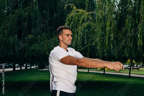 Young sportsman doing stretching exercise, preparing for afrernoon training in the park. Fitness, sport, lifestyle concept photo