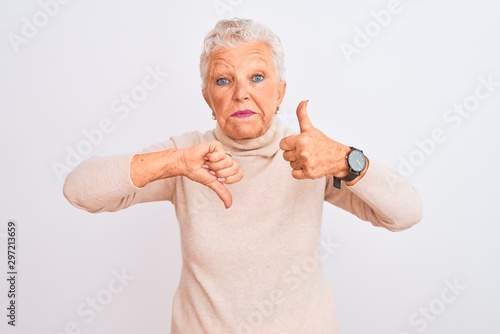 Senior grey-haired woman wearing turtleneck sweater standing over isolated white background Doing thumbs up and down, disagreement and agreement expression. Crazy conflict