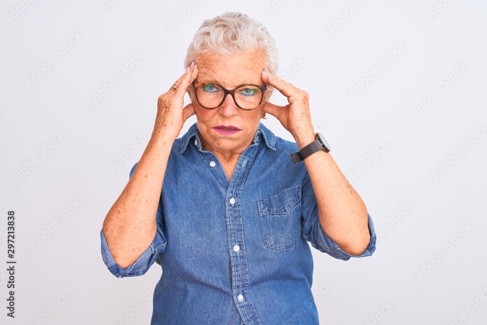 Senior grey-haired woman wearing denim shirt and glasses over isolated white background with hand on headache because stress. Suffering migraine. Senior grey-haired woman wearing denim shirt and glasses over isolated white background with hand on headache because stress. Suffering migraine.