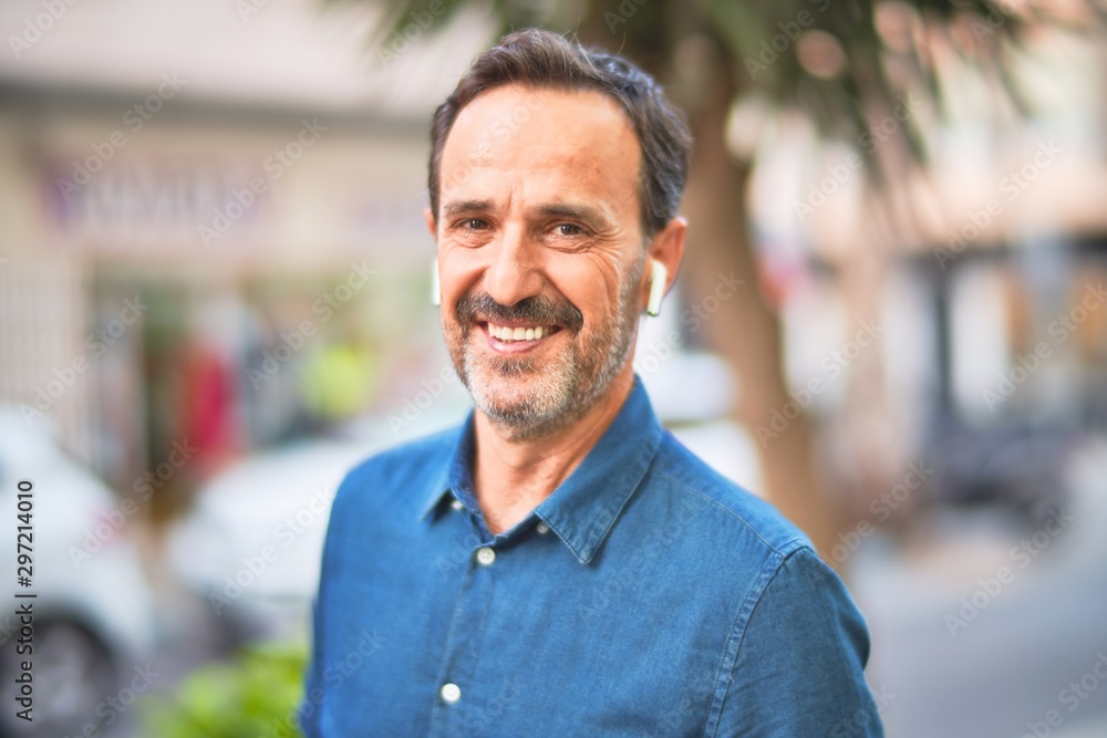 Middle age handsome businessman standing on the street listening to music using earphones smiling Middle age handsome businessman standing on the street listening to music using earphones smiling