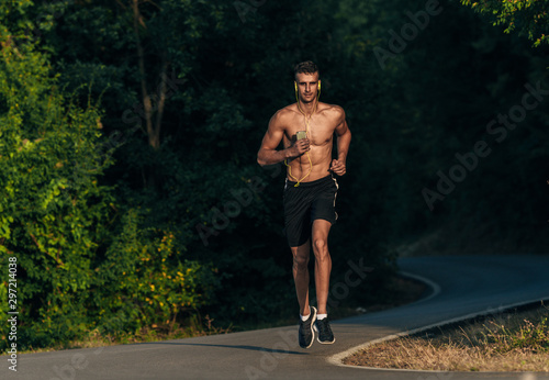 Sporty shirtless man jogging with mobile in his hands