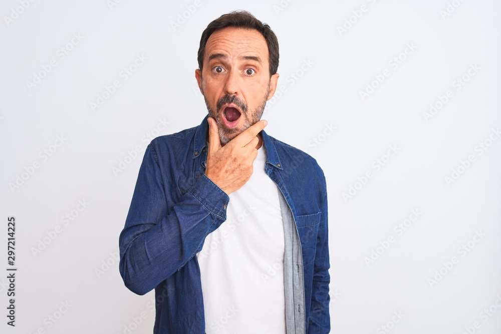 Middle age handsome man wearing blue denim shirt standing over isolated white background Looking fascinated with disbelief, surprise and amazed expression with hands on chin Middle age handsome man wearing blue denim shirt standing over isolated white background Looking fascinated with disbelief, surprise and amazed expression with hands on chin