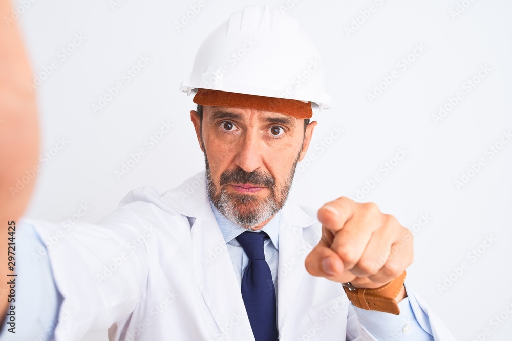 Middle age engineer man wearing helmet make selfie over isolated white background pointing with finger to the camera and to you, hand sign, positive and confident gesture from the front Middle age engineer man wearing helmet make selfie over isolated white background pointing with finger to the camera and to you, hand sign, positive and confident gesture from the front