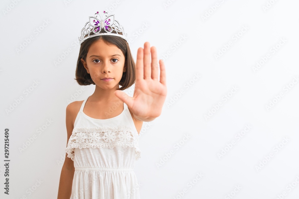 Beautiful child girl wearing princess crown standing over isolated white background doing stop sing with palm of the hand. Warning expression with negative and serious gesture on the face. Beautiful child girl wearing princess crown standing over isolated white background doing stop sing with palm of the hand. Warning expression with negative and serious gesture on the face.
