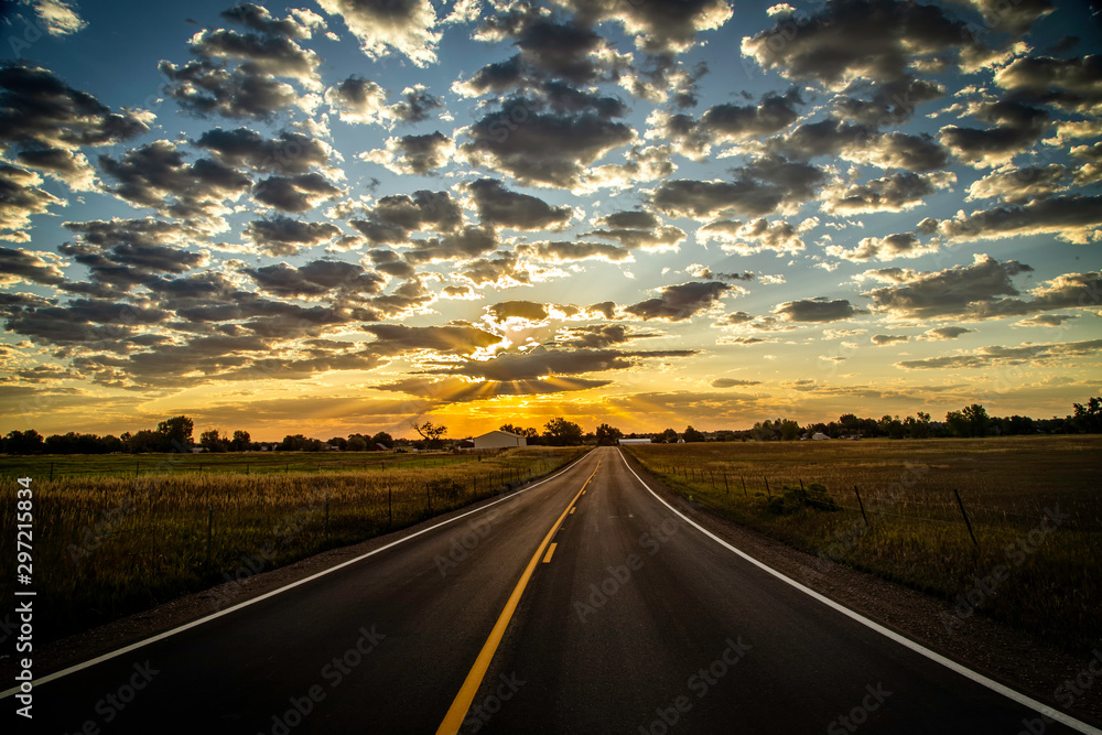 Paved Road leading into the Horizon as sun rays beam out of the clouds