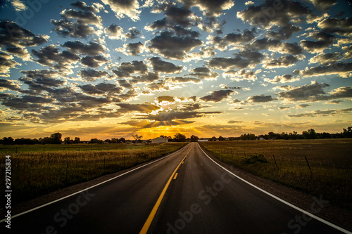 Paved Road leading into the Horizon as sun rays beam out of the clouds