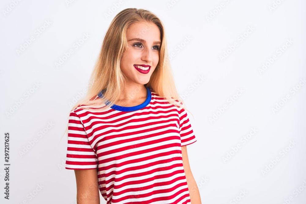 Young beautiful woman wearing red striped t-shirt standing over isolated white background looking away to side with smile on face, natural expression. Laughing confident. Young beautiful woman wearing red striped t-shirt standing over isolated white background looking away to side with smile on face, natural expression. Laughing confident.
