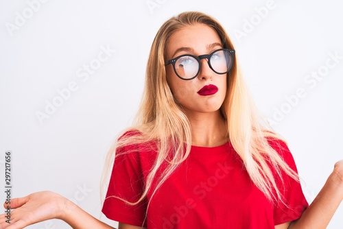 Young beautiful woman wearing red t-shirt and glasses standing over isolated white background clueless and confused expression with arms and hands raised. Doubt concept.