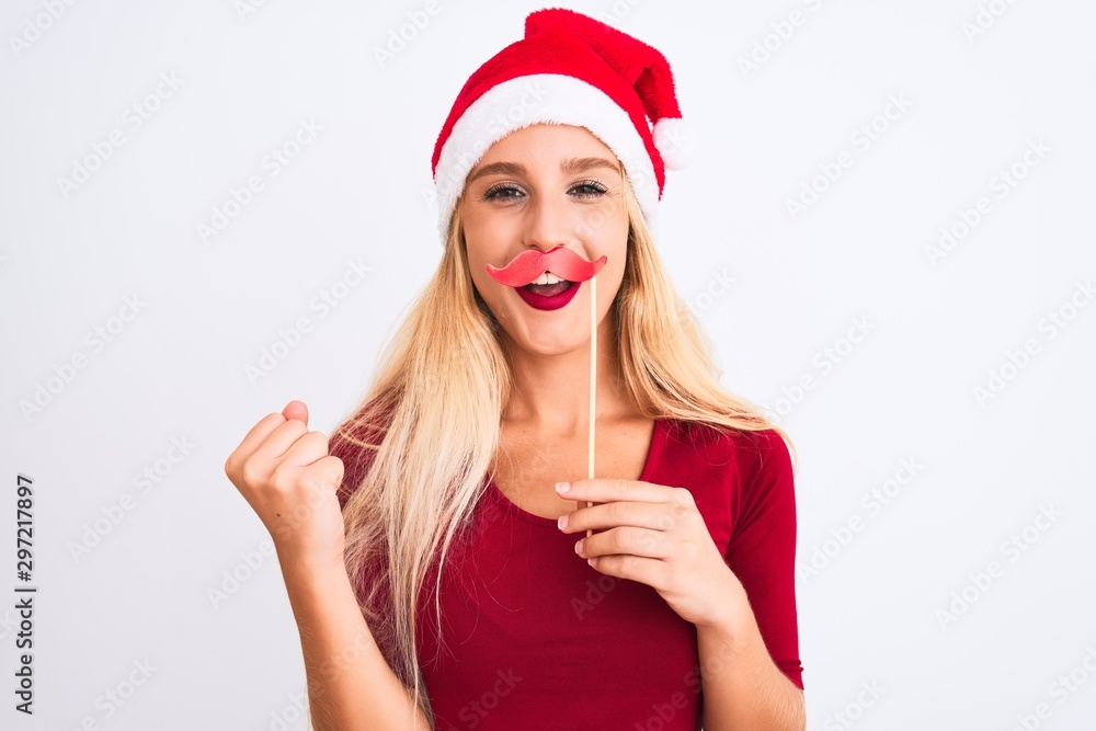Woman wearing Christmas Santa hat holding fanny mustache over isolated white background screaming proud and celebrating victory and success very excited, cheering emotion Woman wearing Christmas Santa hat holding fanny mustache over isolated white background screaming proud and celebrating victory and success very excited, cheering emotion