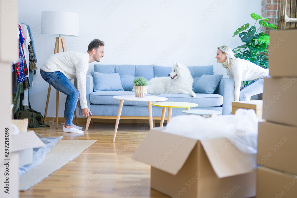 Obraz premium Young beautiful couple with animal moving sofa at new home around cardboard boxes